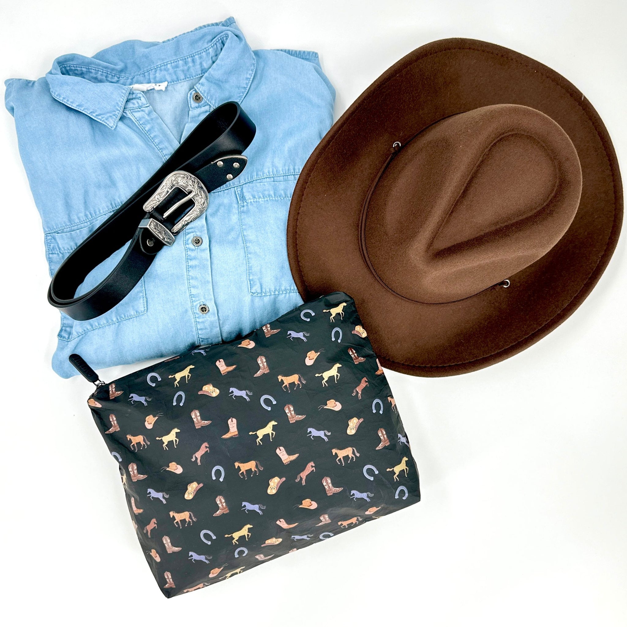 Black equestrian zipper pouch lying with brown cowboy hat, black belt, and denim shirt