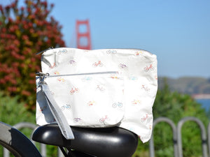 White mini zipper pouch with colorful bicycles pattern sitting on top of bike seat