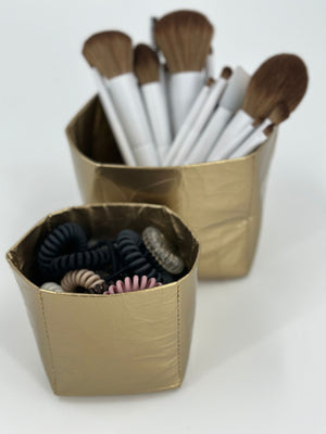 Set of two gold cup organizers with makeup brushes and hair ties inside