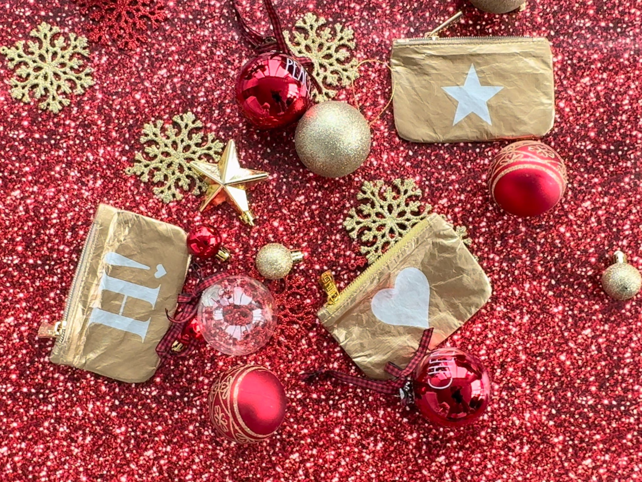 Three gold gift card holder pouches with star and heart laying on red glitter holiday background