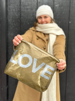 Woman in tan coat and scarf holding a gold zipper pouch in front of her