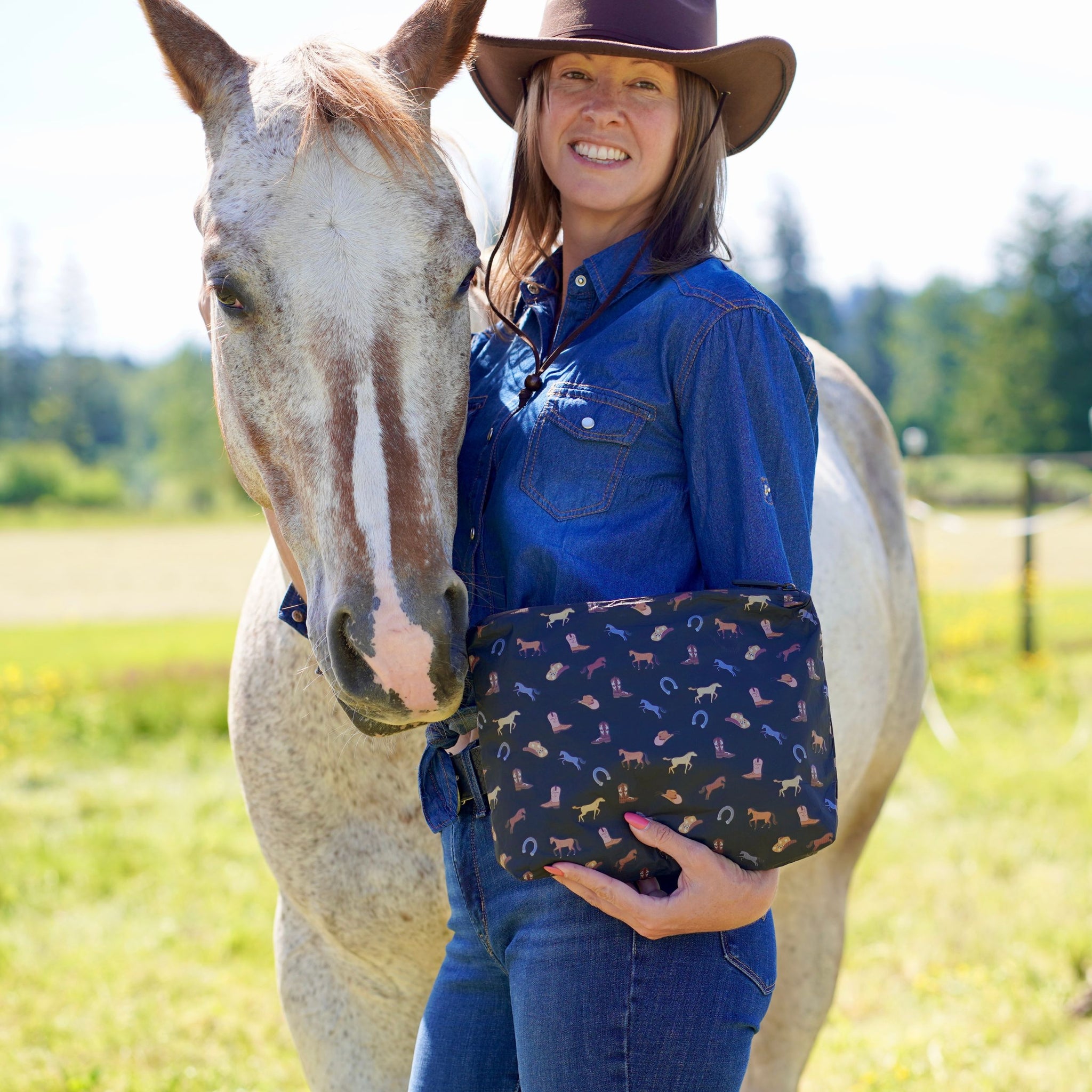 Smiling woman standing next to white horse with an equestrian pattern clutch bag