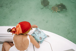 Woman with a sea green turtle patterned zipper pouch overlooking sea turtles in ocean