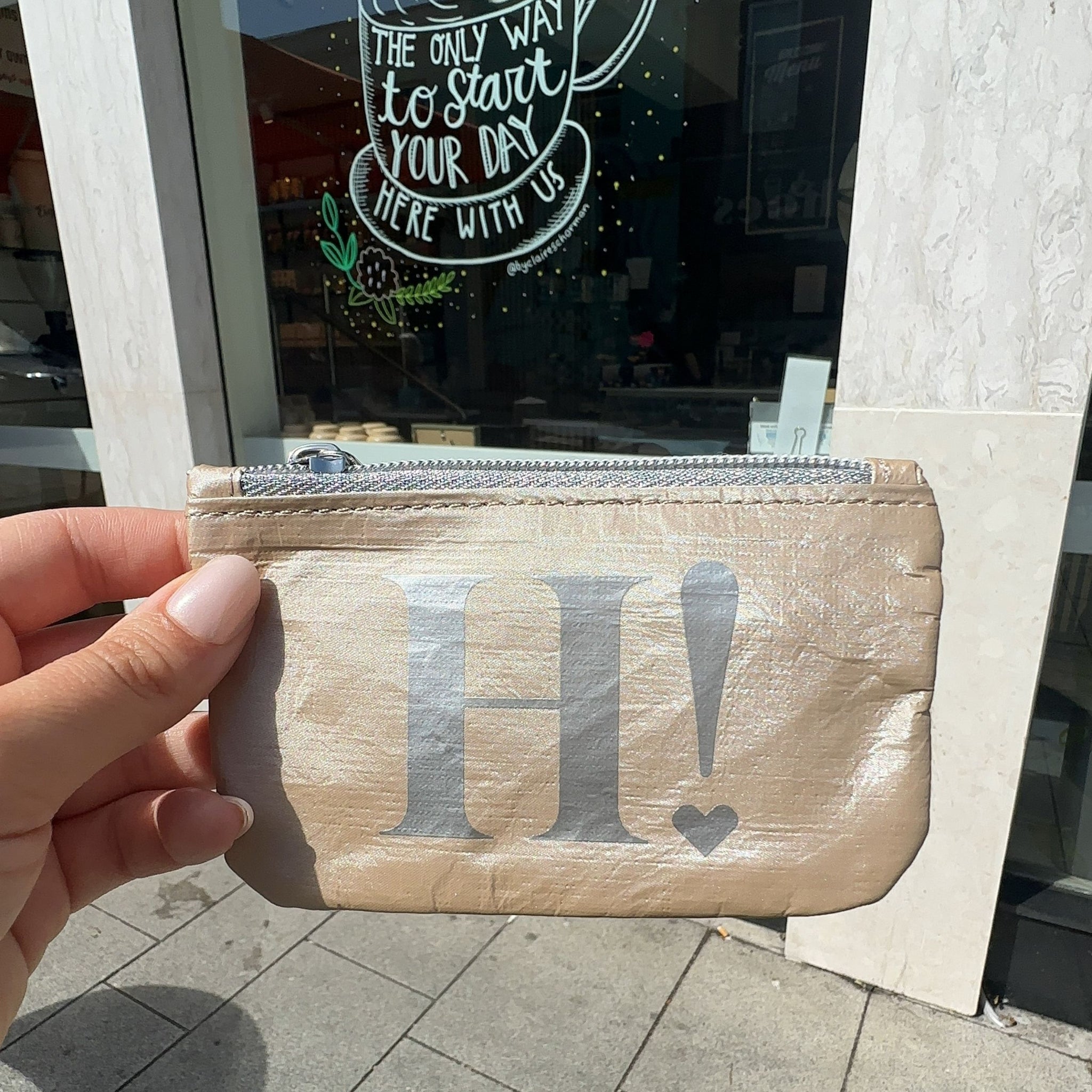 Shimmer beige mini zipper pouch held up in front of coffee shop