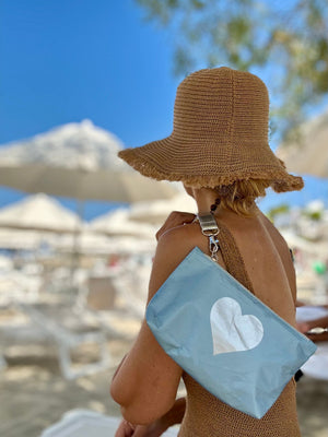 Woman outside in beach hat holding shimmer ice blue with silver heart mini pouch