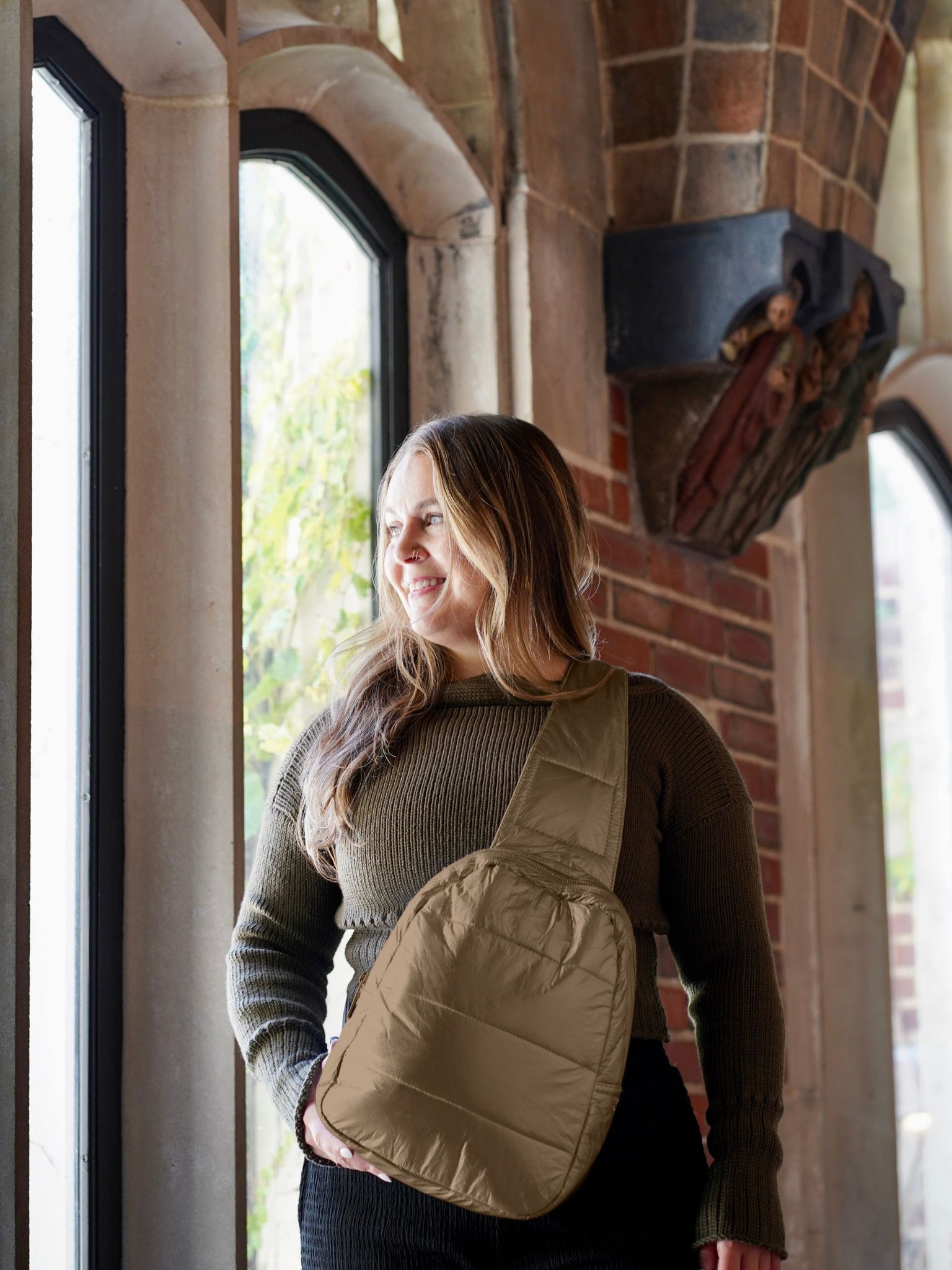 Woman standing near brick wall wearing shimmer bronze crossbody backpack