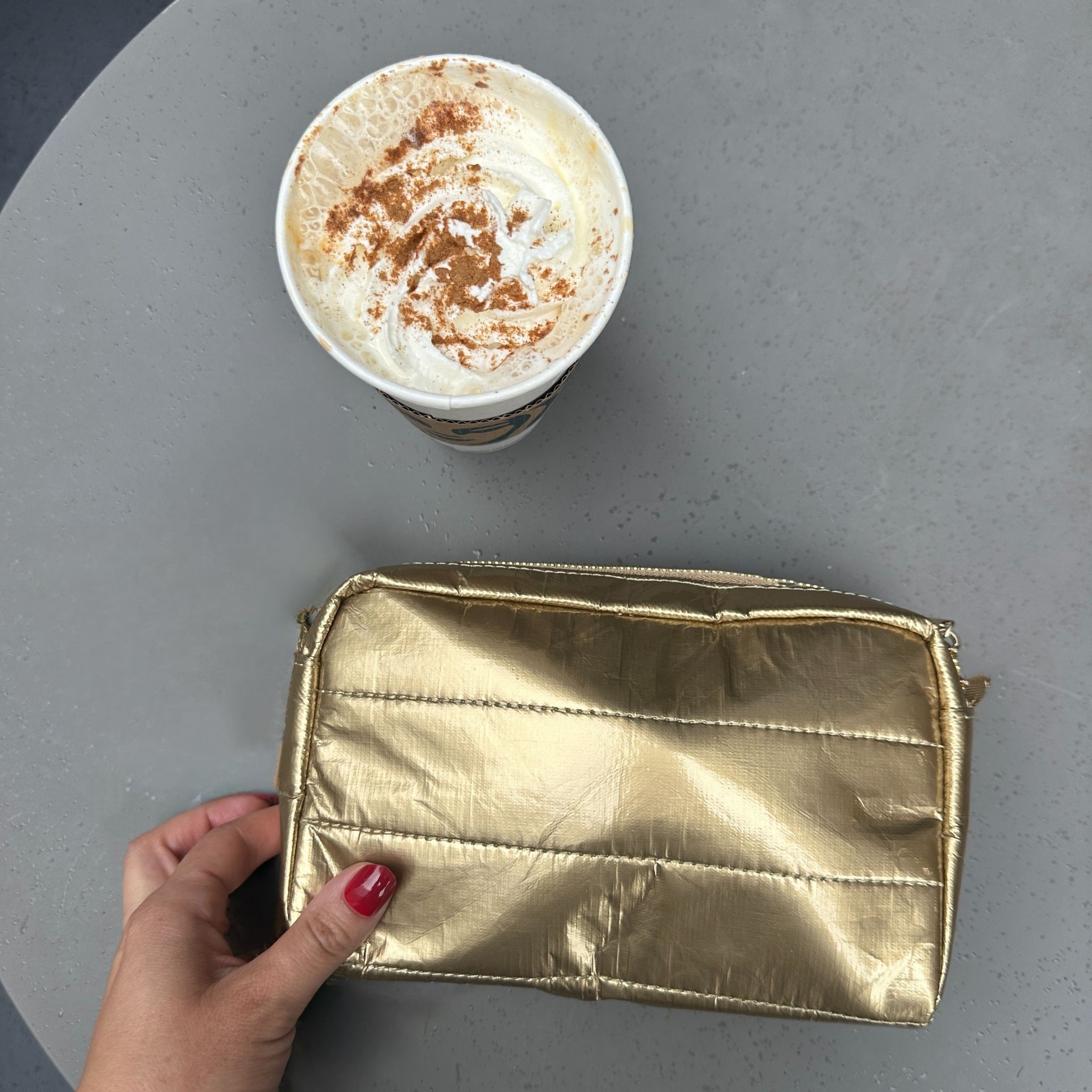 Gold puffer mini clutch on table next to a cup of coffee