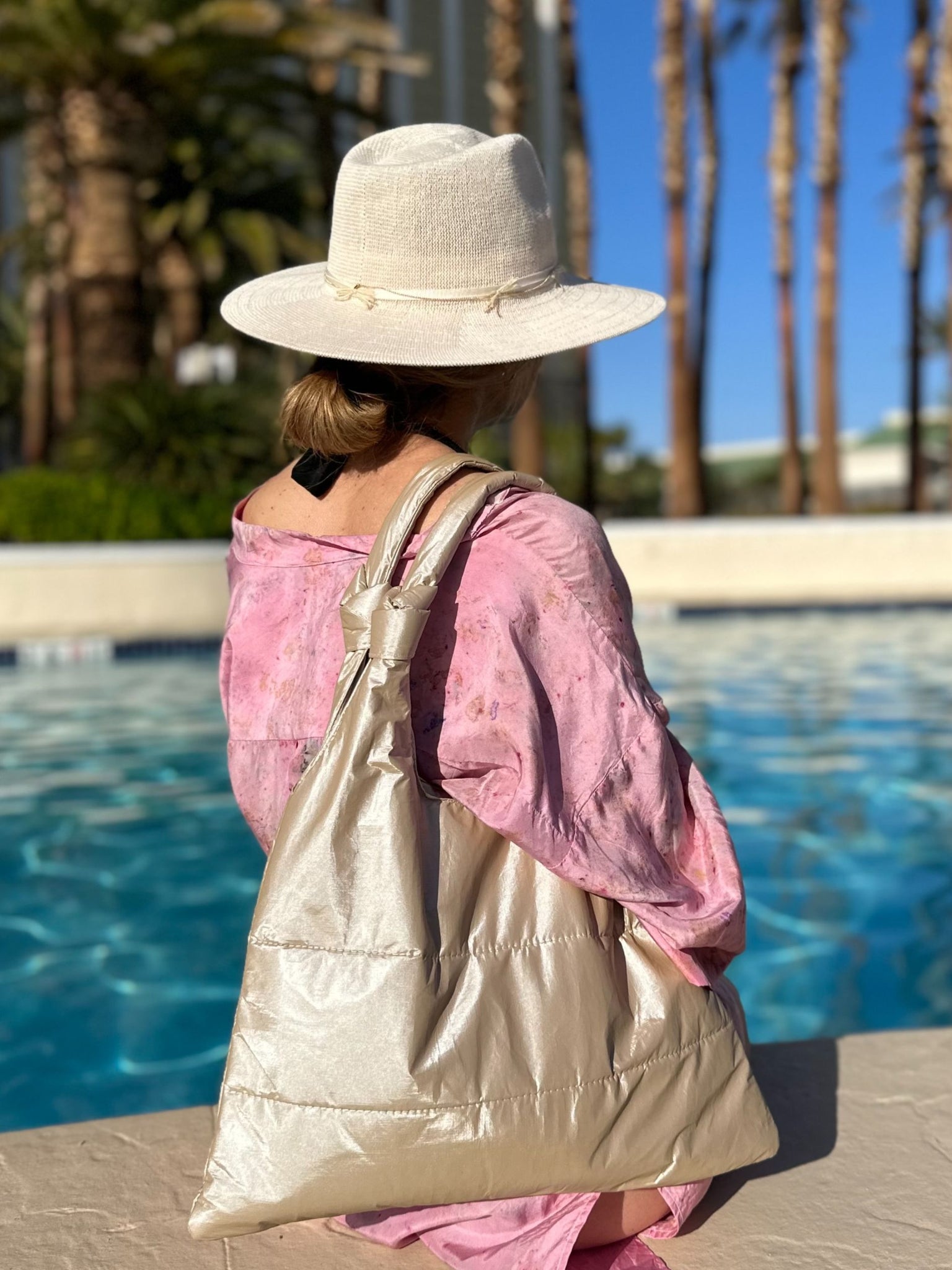 Woman sitting at edge of pool with shimmer beige puffer tote handbag on shoulder