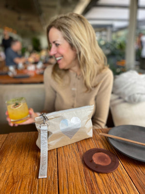 Woman sitting at a bar table with a shimmer beige and silver heart wristlet