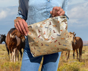 Woman standing with horses holding beige zipper pouch with equestrian pattern