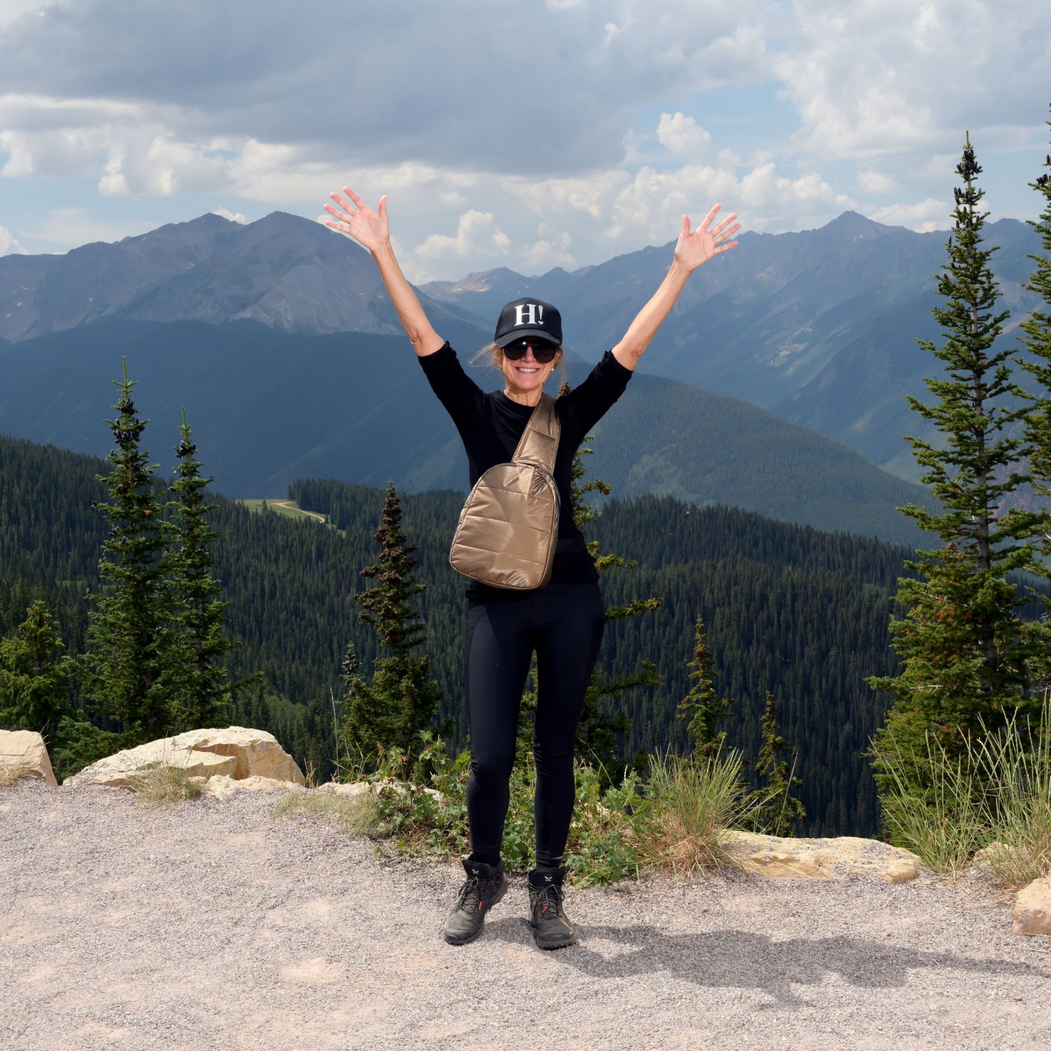 Woman standing in front of mountains wearing shimmer bronze crossbody backpack