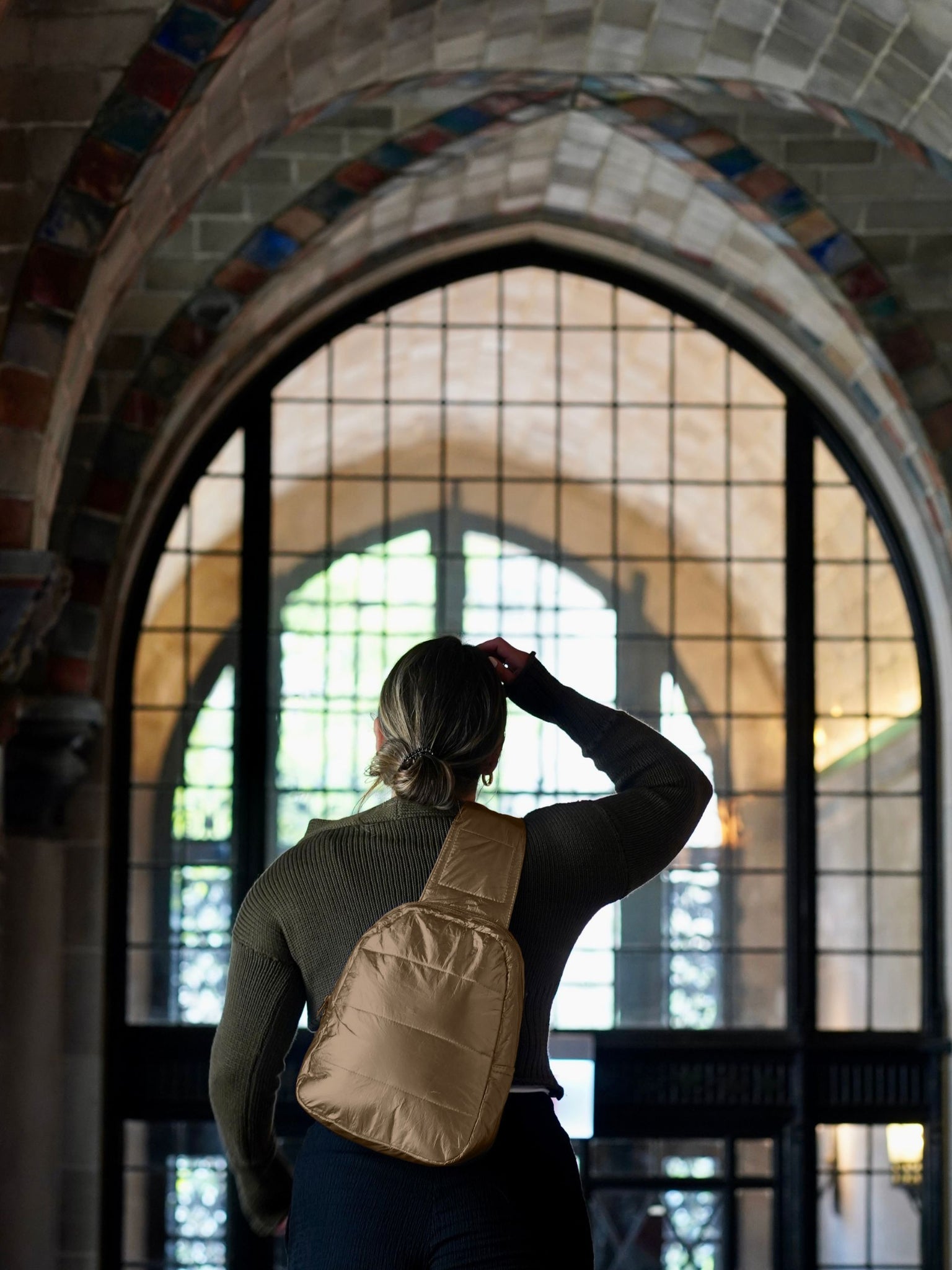 Woman standing inside a chapel wearing shimmer bronze crossbody backpack