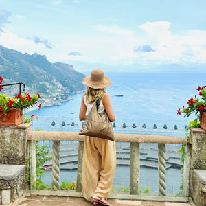 Woman standing in front of ocean and mountains in Italy with shimmer bronze shoulder purse