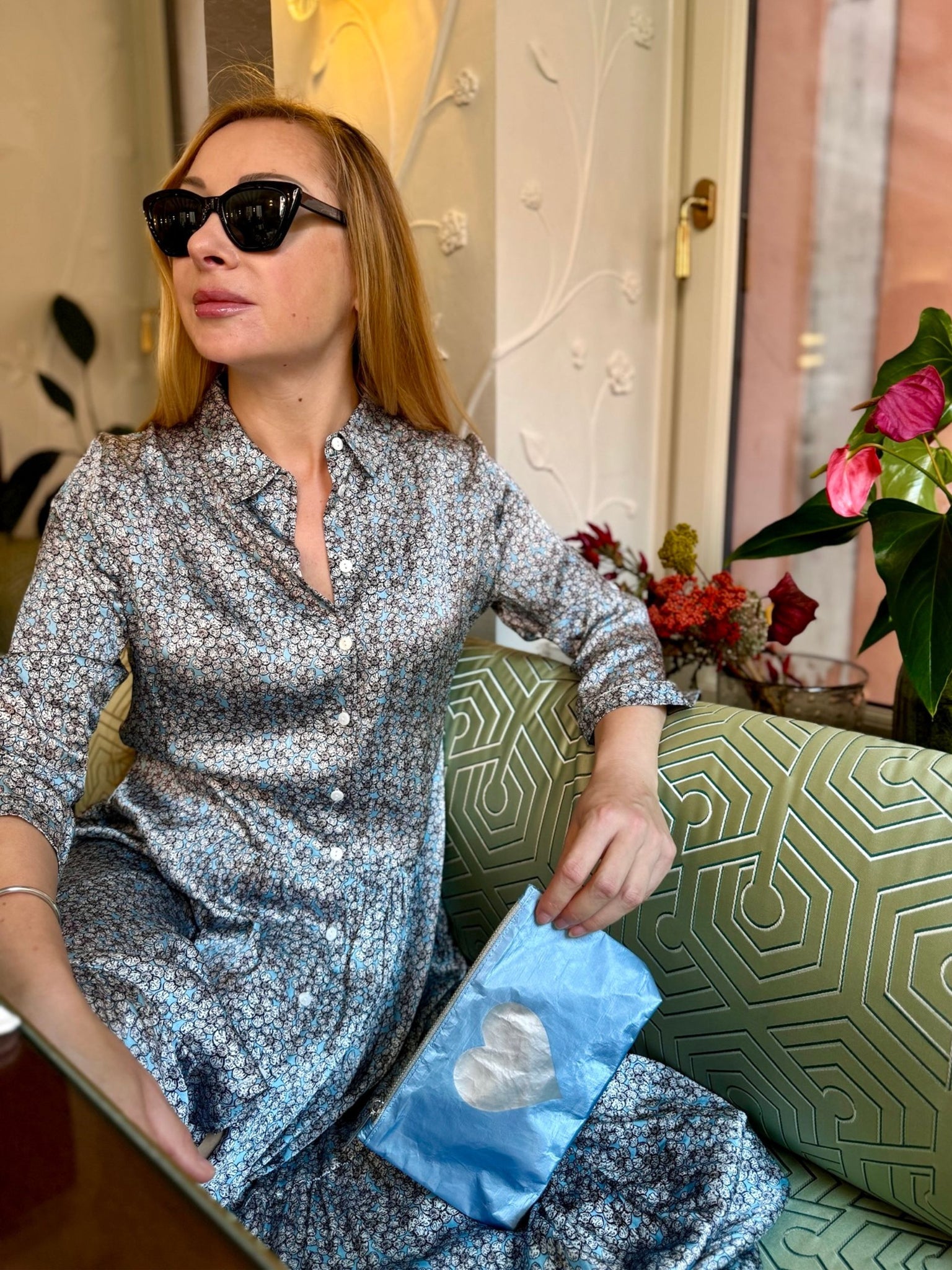 Woman in a floral dress holding a shimmer ice blue mini zipper clutch with silver heart emblem