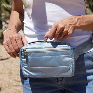 Woman unzipping a shimmer ice blue puffer fanny pack with silver zippers