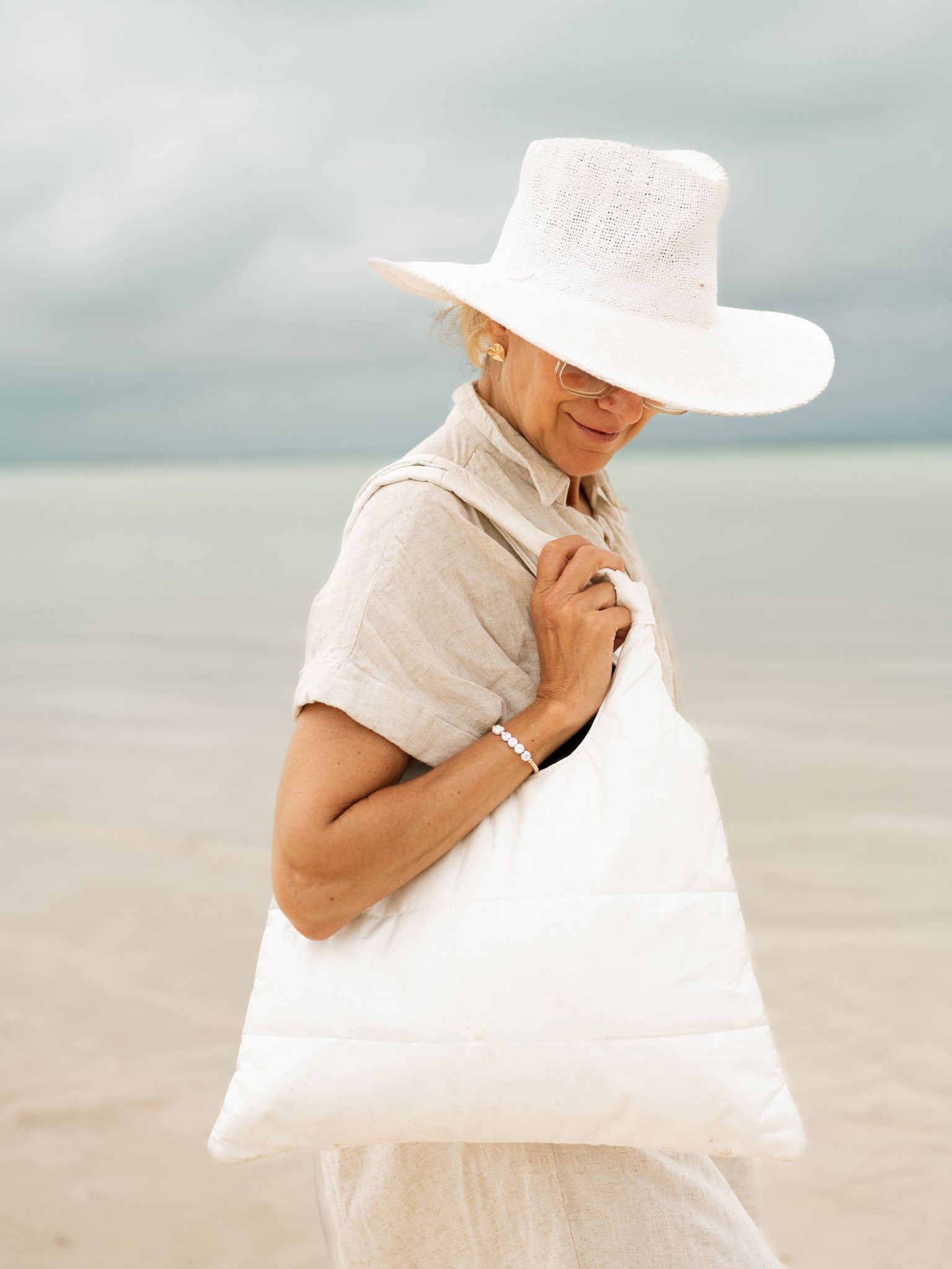 Woman on a beach with white hat and shimmer white puffer purse tote on shoulder