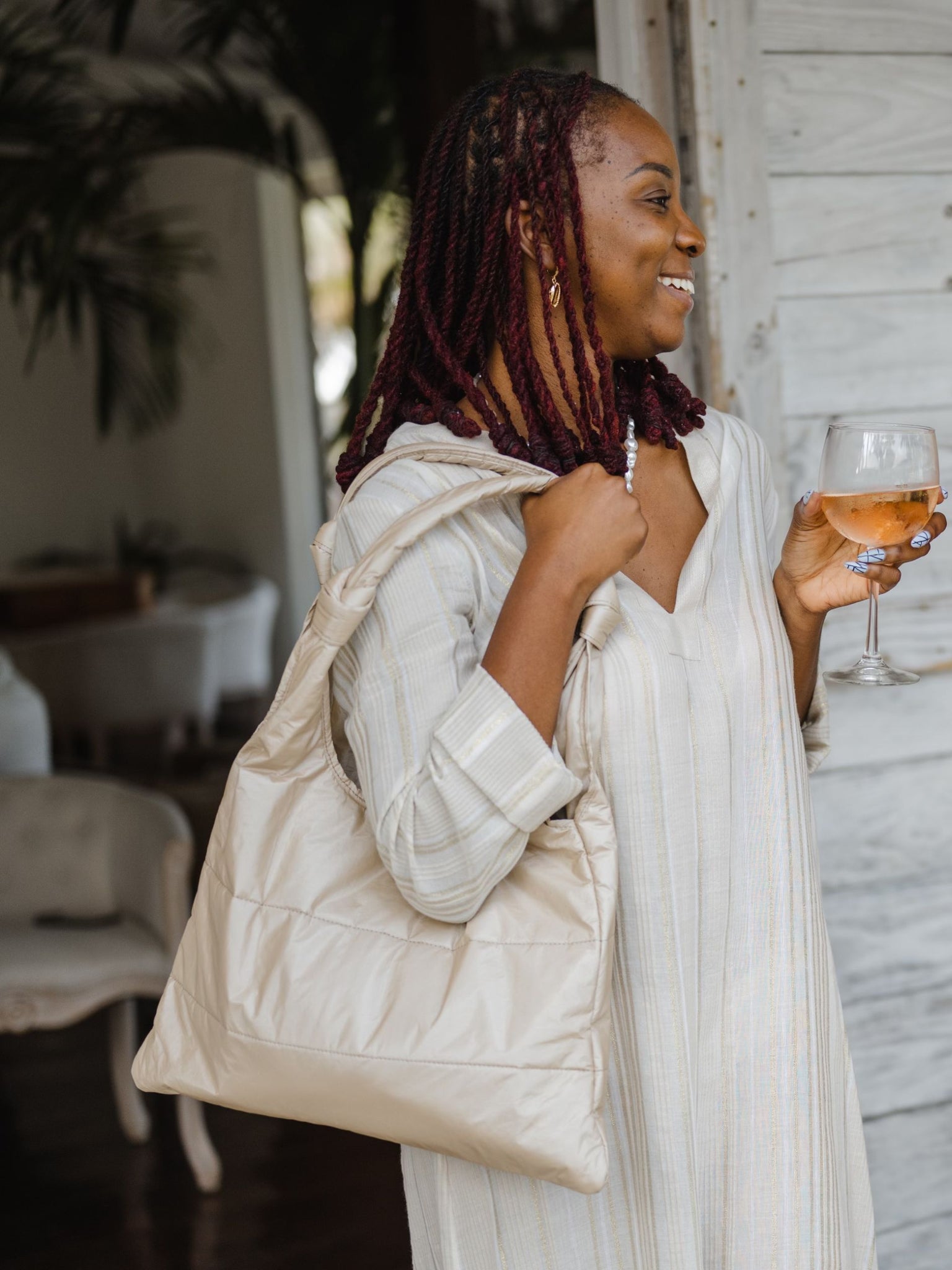 Woman standing holding a glass of wine and shimmer beige puffer tote on shoulder