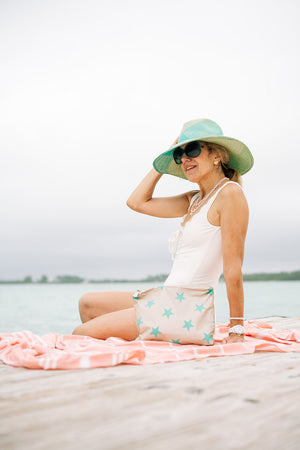 Woman sitting on the beach with a beige and green stars zipper pouch