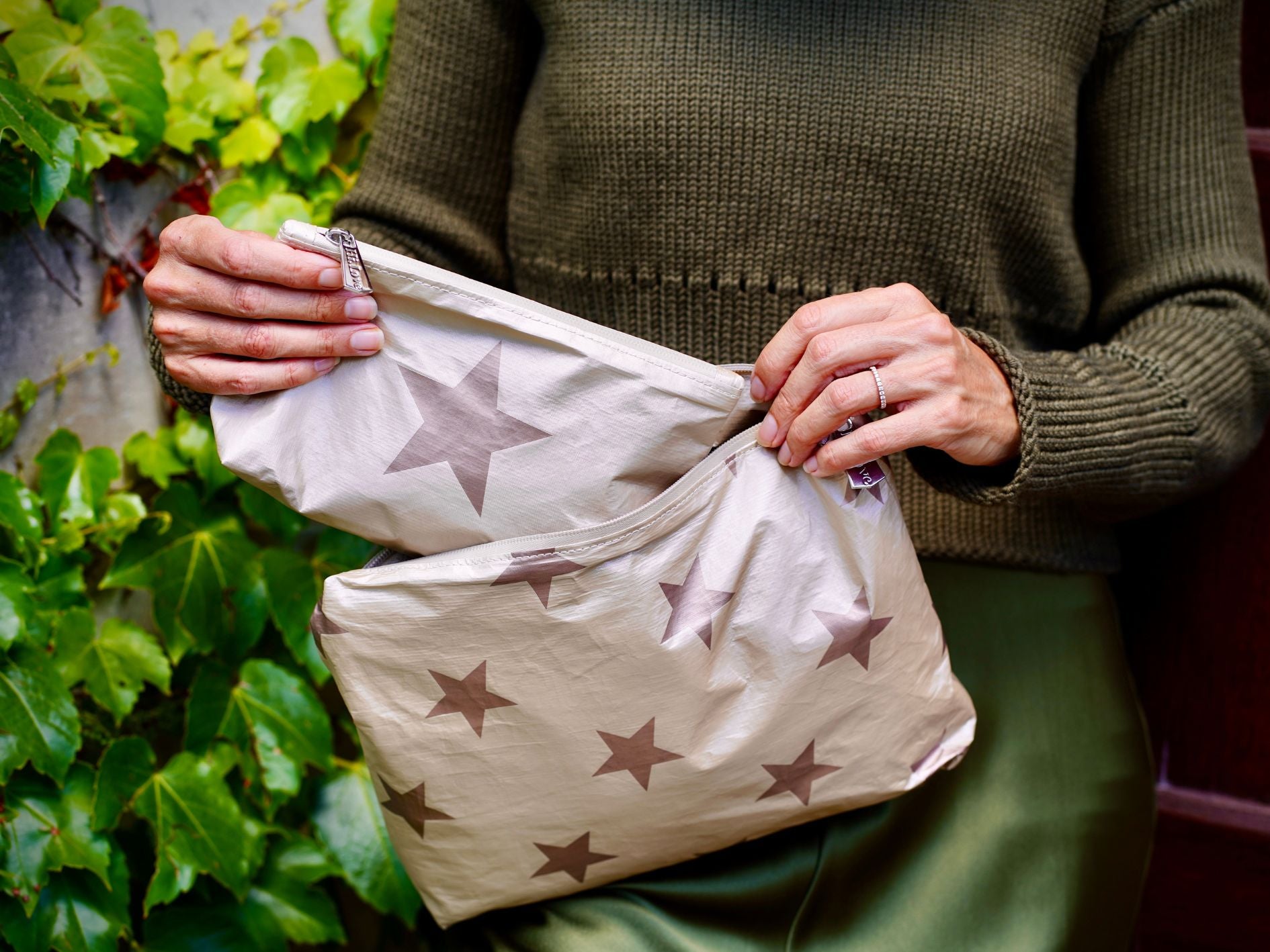 Woman in green dress holding medium shimmer beige with bronze stars pouch and mini beige with bronze star pouch