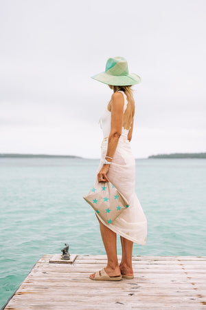 Woman standing on a dock holding a beige and stars zipper pouch