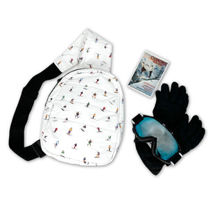 White with skiers pattern crossbody backpack with ski goggles, gloves, and brochure around it