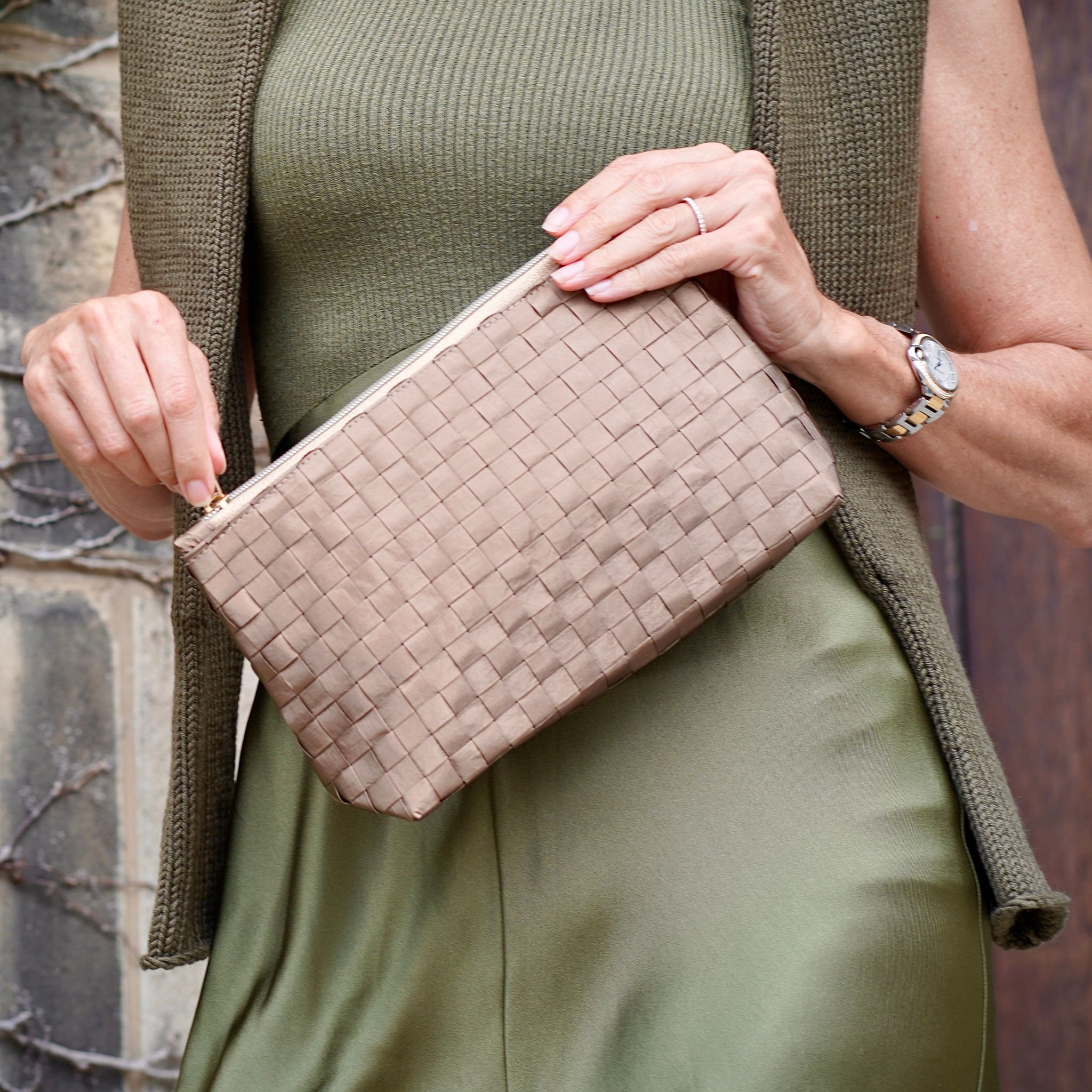 Woman in army green dress holding woven shimmer bronze zipper clutch