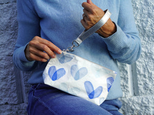 Woman holding white zip wristlet with shades of blue hearts and silver wrist strap