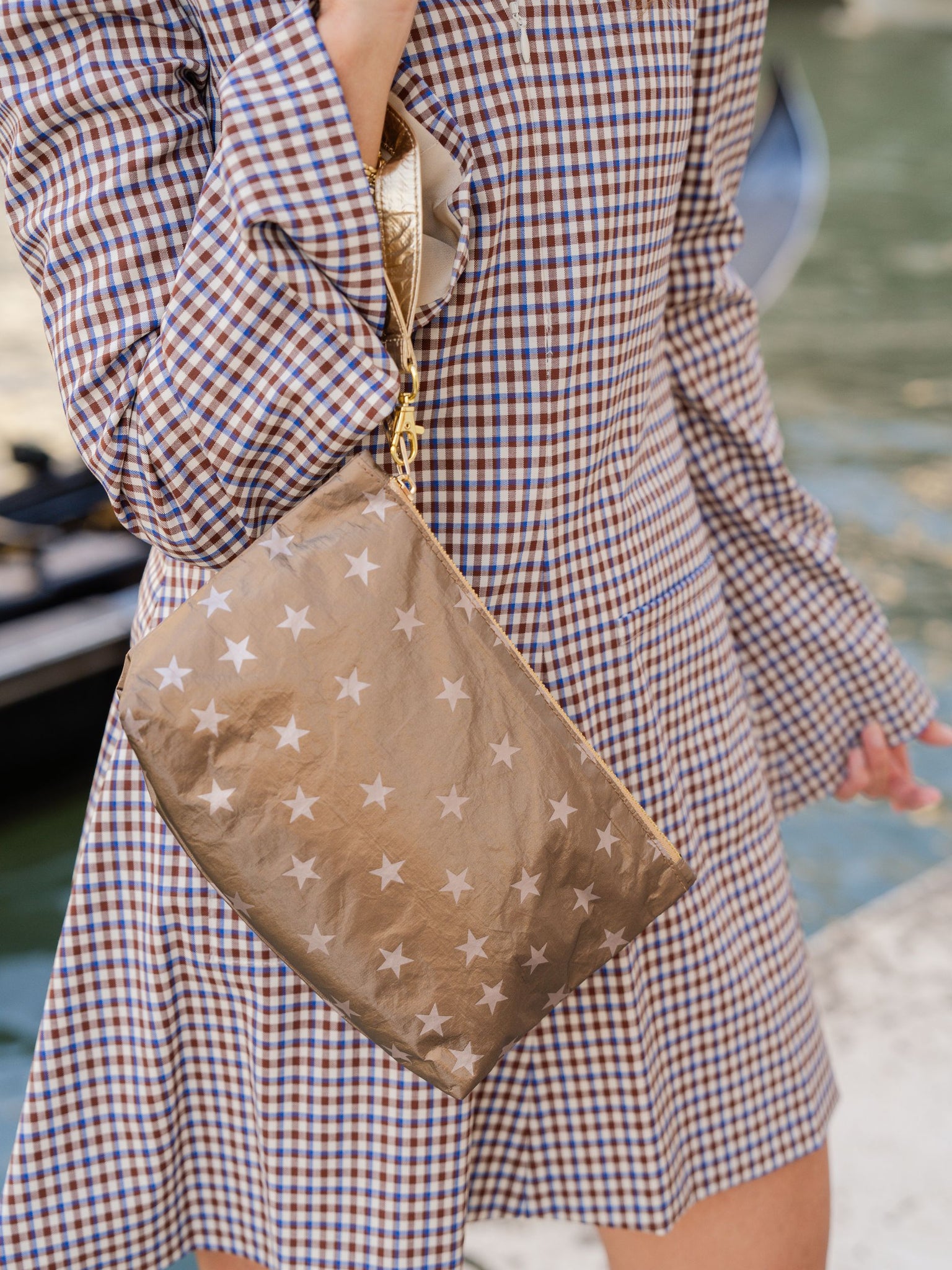 Woman in brown, blue, and white checkered dress wearing shimmer bronze stars wristlet