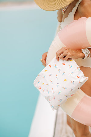 Woman at poolside holding white zipper pouch with swimmers and divers pattern