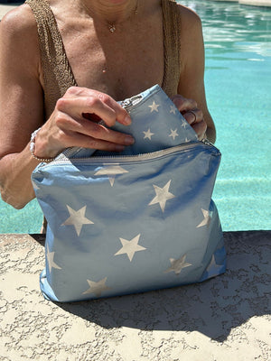 Woman standing in a pool holding shimmer ice blue with silver stars zipper pouches